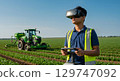 Young man wearing virtual reality headset farm field with tractor, exploring technology with 129747092