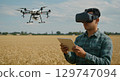 Man wearing virtual reality headset controlling drone with tablet in wheat field 129747094