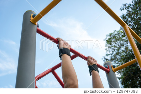 Man doing pull ups workout on the steel bar in the park. 129747388