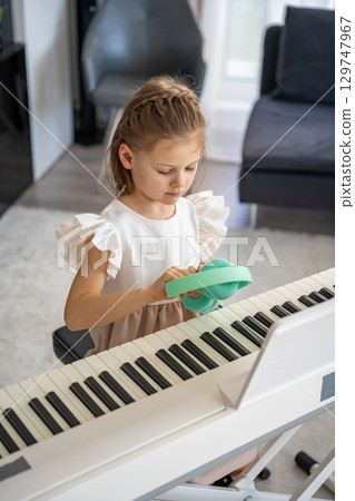 Little girl practicing piano with wireless headphones at home. Early childhood development through modern and focused music education. 129747967