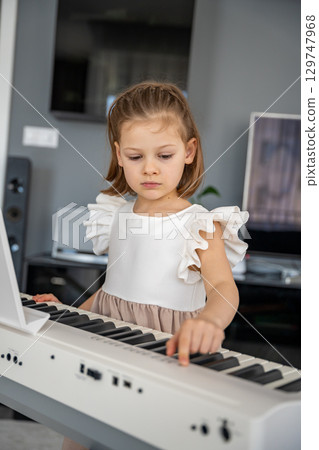 Little girl preparing to play piano at home in the living room. Calm moment of focus and anticipation before music practice in a cozy family space. Little girl preparing to play piano at home in the living room. Calm moment of focus and anticipation before music practice in a cozy family space. 129747968