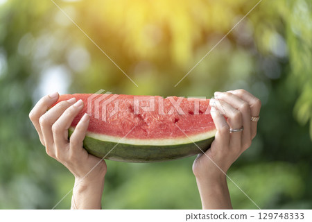 Women eat red watermelon organic hand holding red fruit high vitamins outdoor on tropical beach summertime. Young asian women smile enjoy eating tropical fruit happy time smile face. Female vegan 129748333