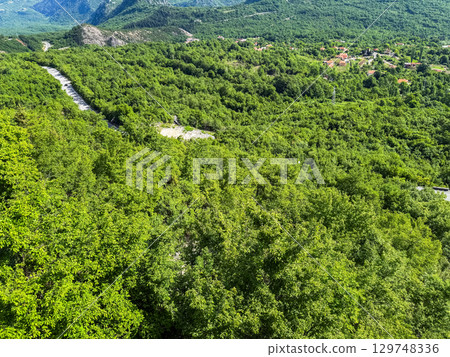Gravel road winding through lush mountain forest with rocky peaks on the horizon. Adventure, exploration, and peaceful remoteness in wild Montenegro. 129748336