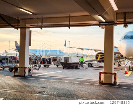 Airport ground crew loading luggage at sunrise. Travel logistics, aviation operations, and early morning airport workflow on the tarmac. Airport ground crew loading luggage at sunrise. Travel logistics, aviation operations, and early morning airport workflow on the tarmac. 129748355