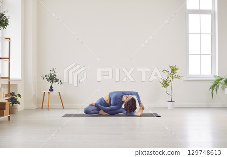 Sporty beautiful young woman practicing yoga, doing Janu Sirsasana, Head-to-Knee Forward Bend Pose 129748613