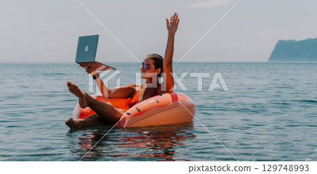 Laptop, Beach, Work - Woman on inflatable ring working on her laptop in the ocean. 129748993