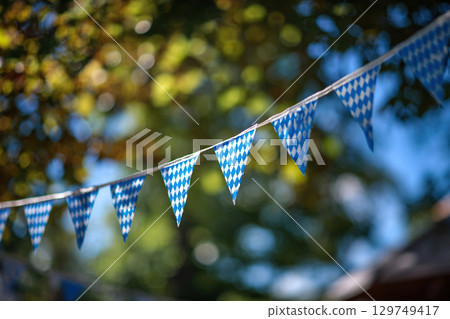 Oktoberfest decoration. Blue and white triangular flags in the form of a garland between the trees. 129749417