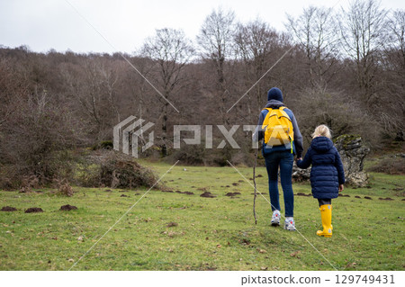 Father, daughter hiking woodland trail, yellow boots matching backpacks, winter landscape surrounding them Father, daughter hiking woodland trail, yellow boots matching backpacks, winter landscape surrounding them 129749431