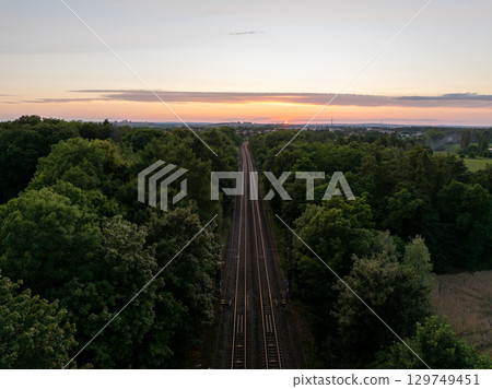 The sun sets over railway tracks disappearing into a forest near Prague, Czechia 129749451