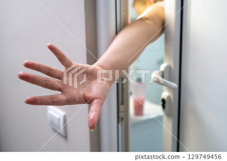 Exhausted female extending hand through bathroom doorway, seeking assistance post exercise or bathing 129749456