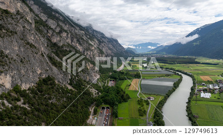Breathtaking aerial view of a highway and river winding through a valley, surrounded by mountains, fields, and forests in Tyrol, Austria 129749613