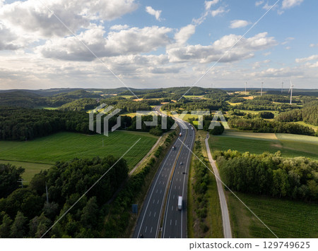 Aerial view of highway a9 crossing the Bavarian countryside near pegnitz, with trucks driving on asphalt road, green fields, forests and wind turbines in background 129749625