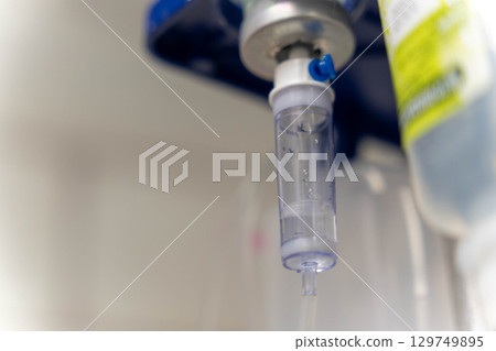 Intravenous therapy delivering saline solution through drip chamber in hospital setting Intravenous therapy delivering saline solution through drip chamber in hospital setting 129749895