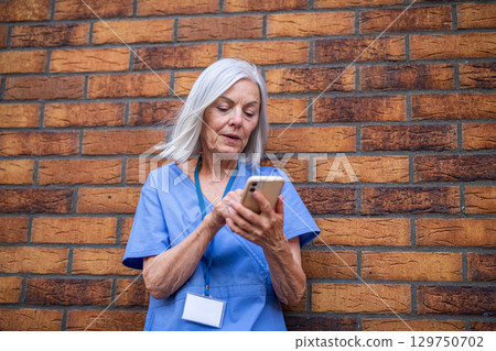 Older nurse resting during long hospital shift, making phone call 129750702