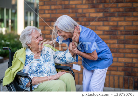 Tender moment between older caregiver and senior female patient in wheelchair. 129750703