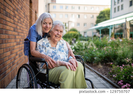 Aging woman in wheelchair enjoying fresh air with care assistant 129750707