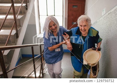 Female healthcare worker helping senior patient walking up the stairs. Female healthcare worker helping senior patient walking up the stairs. 129750712