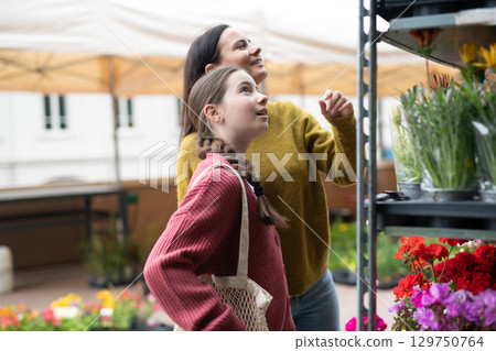 Mother and daughter choosing flowers at market. 129750764