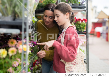 Mother and daughter choosing flowers at market. 129750765