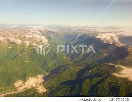 Sunlit mountain valley with dramatic shadows and cloud layers. Early morning light, topographic contrast, and aerial perspective of natural landscape. Sunlit mountain valley with dramatic shadows and cloud layers. Early morning light, topographic contrast, and aerial perspective of natural landscape. 129751466