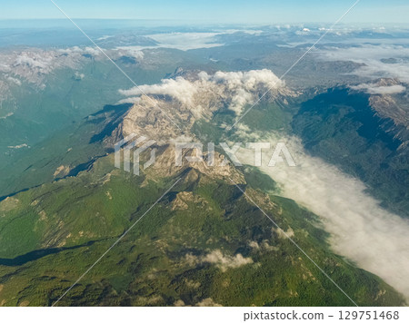 Rocky mountain ridge with cloud stream cutting through valley. Majestic aerial view of natural formations, elevation, and weather movement. 129751468