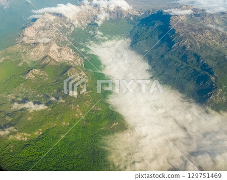 Mountain peaks and forest valley under flowing cloud river. Aerial perspective, dramatic topography, and natural contrast of textures and elevation. Mountain peaks and forest valley under flowing cloud river. Aerial perspective, dramatic topography, and natural contrast of textures and elevation. 129751469