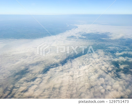 Cloudy aerial view with distant industrial chimney. Weather formation, aerial visibility, and atmospheric depth from airplane flight. Cloudy aerial view with distant industrial chimney. Weather formation, aerial visibility, and atmospheric depth from airplane flight. 129751473