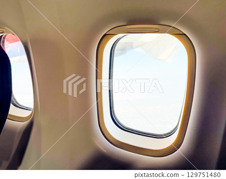 Interior view of airplane windows during flight. Passenger experience, quiet travel moment, and in-flight perspective above the clouds. 129751480