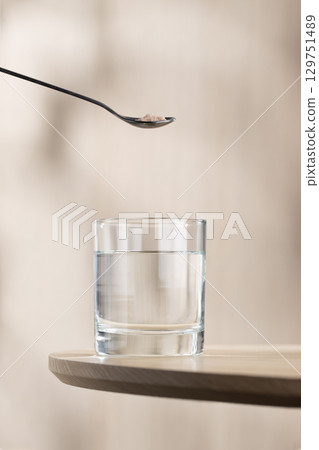 A spoon of Himalayan salt is being added to a glass of drinking water. 129751489