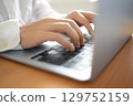 A person operating a laptop. A person wearing a white shirt is typing on a PC keyboard at a desk. 129752159