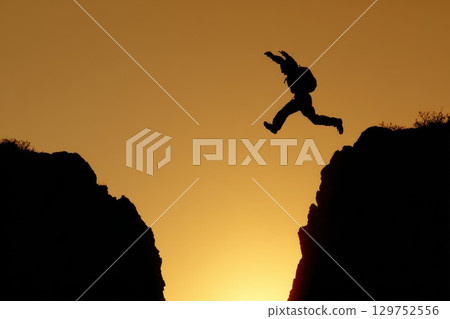 Silhouette of a Person Leaping from One Rock to Another at Sunset 129752556