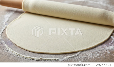 Rolling dough with wooden rolling pin on floured surface for baking 129753495