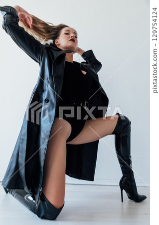 woman in black leather raincoat and latex boots 129754124