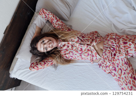 woman in pajamas smiling in bedroom on bed woman in pajamas smiling in bedroom on bed 129754231