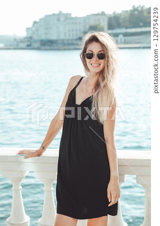 Blonde in a black dress walking on the beach by the sea 129754239