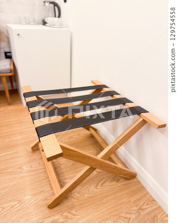 Wooden luggage rack with black straps in hotel room. Travel accommodation, storage, and interior detail. 129754558