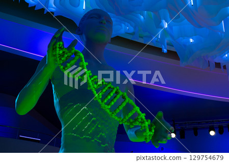 Futuristic sculpture depicting human figure holding glowing green DNA helix, symbolizing the concept of new life and genetic evolution, illuminated by blue neon lights 129754679