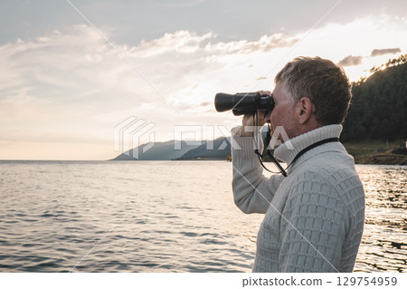 man observing ocean with binoculars on calm day near shoreline at sunset. closeup. 129754959