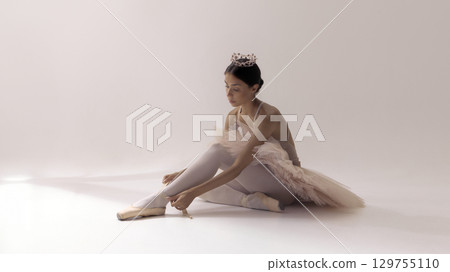 Ballerina in tutu adjusting pointe shoes with serene concentration Ballerina in tutu adjusting pointe shoes with serene concentration 129755110