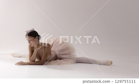 Ballerina in tutu and crown stretching gracefully on stage floor Ballerina in tutu and crown stretching gracefully on stage floor 129755111