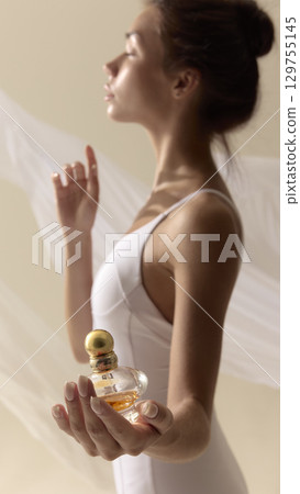Woman in white dress holding perfume bottle with elegance 129755145