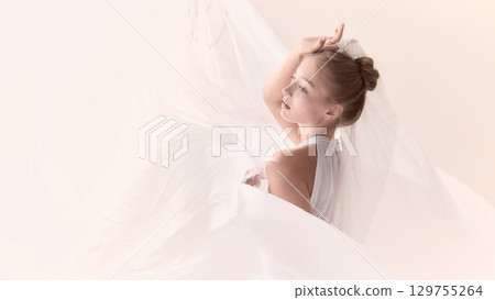 Ballerina in white costume posing with flowing fabric in soft light 129755264
