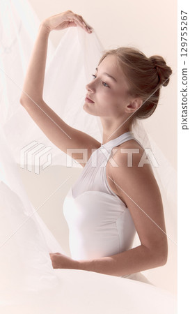 Elegant ballerina in white dress raising arm with fabric gracefully 129755267