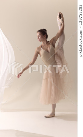 Female ballet dancer stretching leg high in delicate beige costume Female ballet dancer stretching leg high in delicate beige costume 129755282