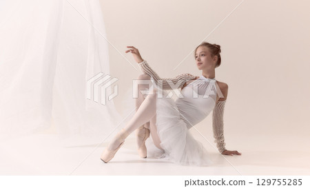 Graceful ballerina in white costume seated elegantly on pointe shoes 129755285