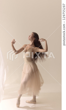Graceful dancer in beige dress spraying perfume with flowing motion 129755287