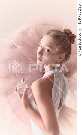 Young ballerina in white dress holding perfume bottle with soft gaze 129755289