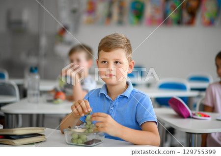 Children in the classroom eating a healthy snack with fruit at their school desks. Children in the classroom eating a healthy snack with fruit at their school desks. 129755399