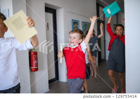 Happy schoolkids in uniforms running down the school hallway. 129755414