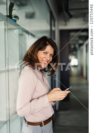 A portrait of businesswoman resting in an office, scrolling on smartphone. 129755448